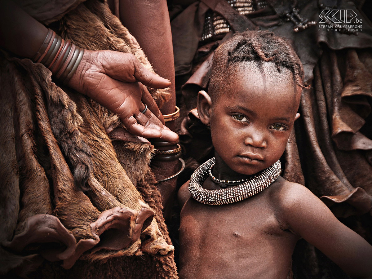 Omangete - Jong Himba meisje Dit kleine schattige Himba meisje staat een beetje vertwijfeld tussen de volwassen vrouwen. Jonge meisjes dragen hun haar in twee dikke vlechten over hun voorhoofd. Stefan Cruysberghs